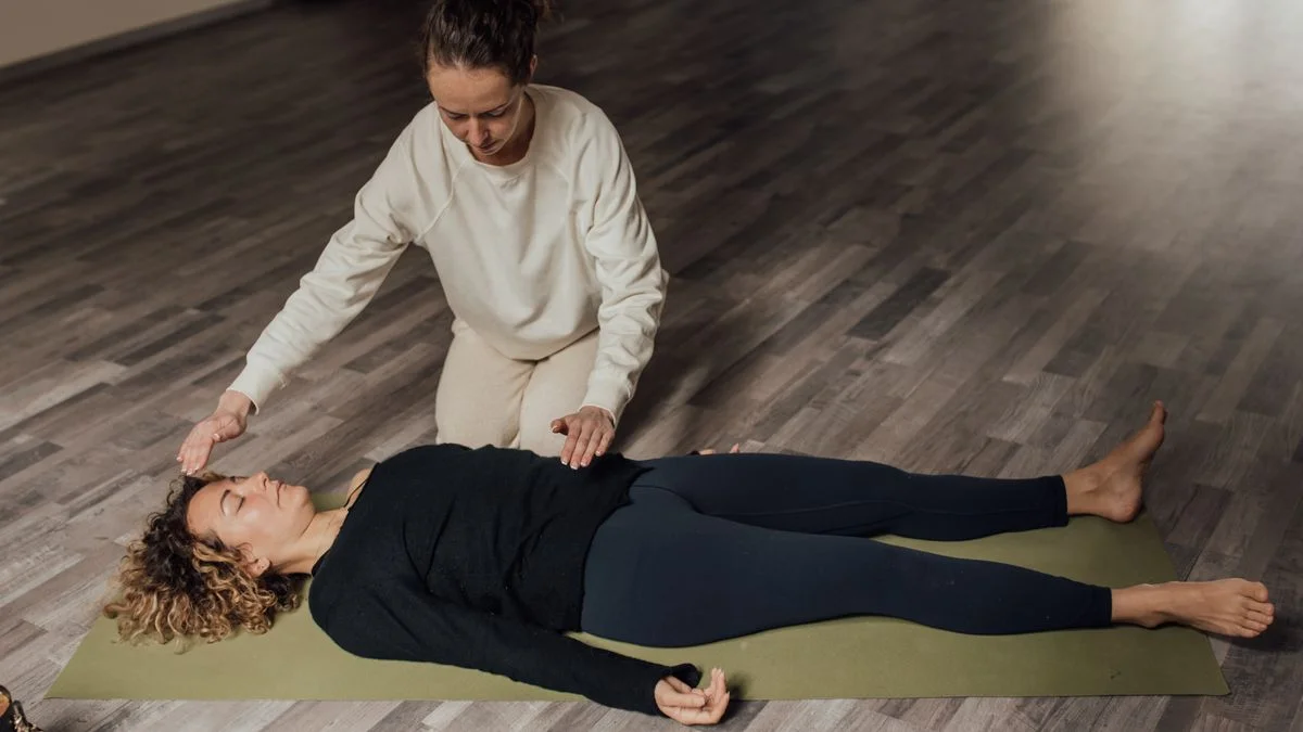 A person lying down with eyes closed in a calm, dimly lit room during a body scan meditation