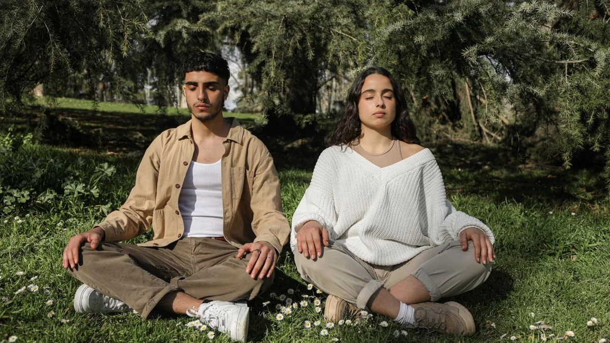 Two people sitting cross-legged together on grass in a park